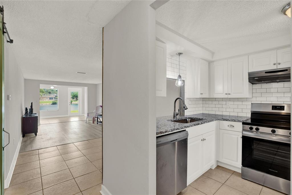 A view from a tiled kitchen with white cabinets into a living area with flooring — 4115 HAMPTON DRIVE UNIT n/a, NEW PORT RICHEY, FL