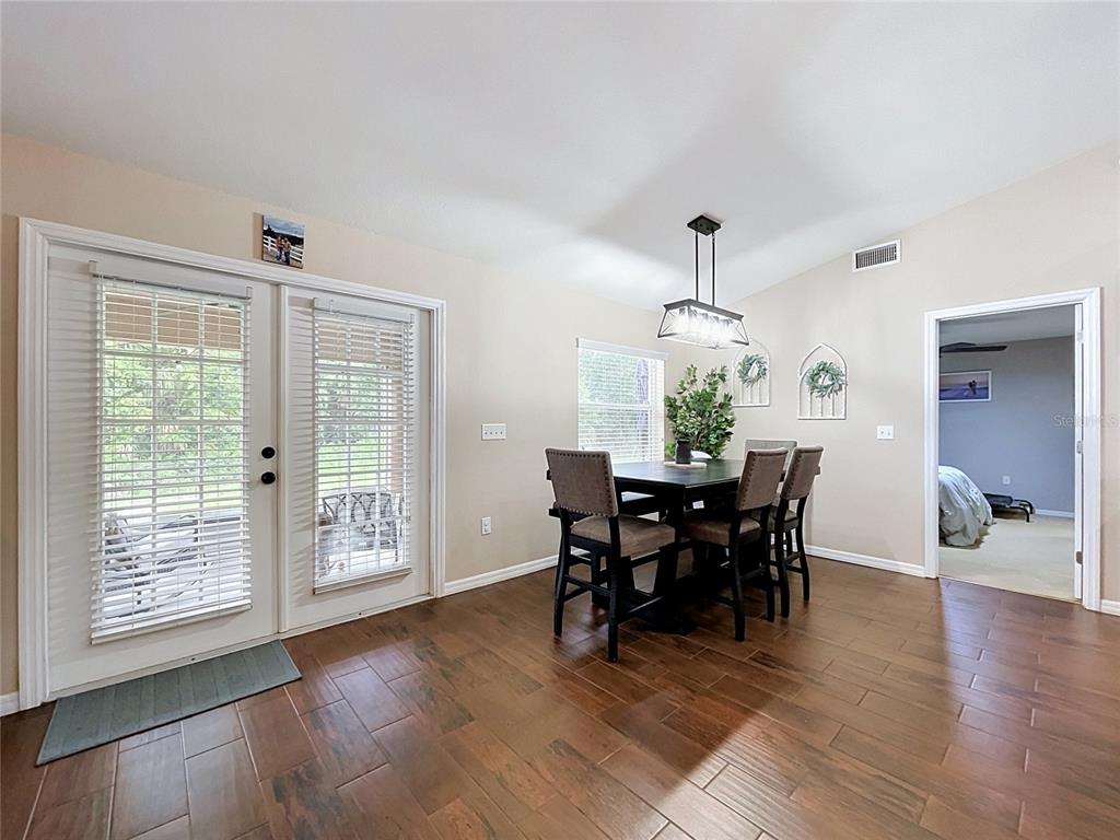 A dining area features wood-look tile flooring, a dark wood table with chairs, and glass doors — 3217 ENCLAVE BOULEVARD, MULBERRY, FL