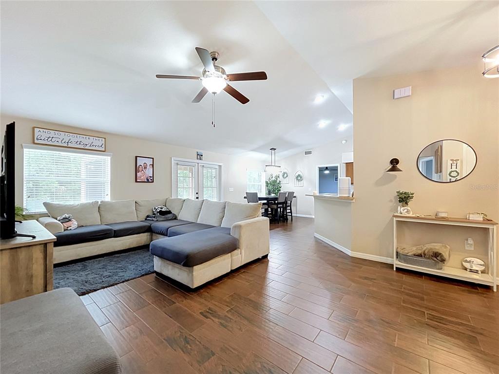 A living room with a sectional sofa, wood-look tile flooring, and an open dining area — 3217 ENCLAVE BOULEVARD, MULBERRY, FL