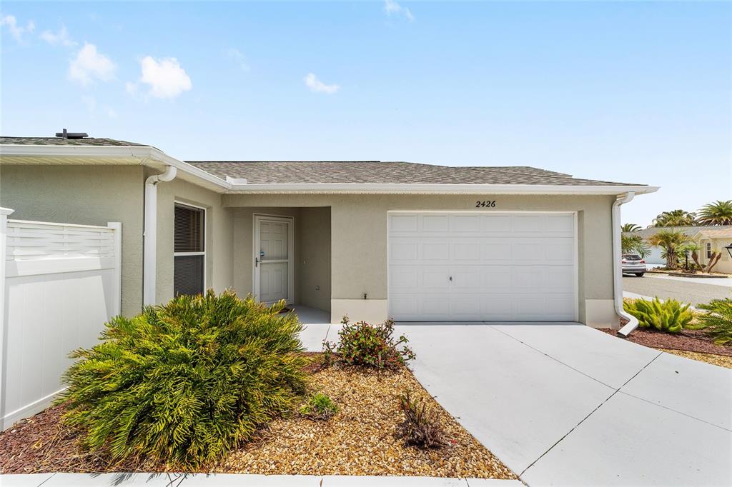 A single-story house exterior features a white garage door, a front entrance, and landscaping — 2426 SAFFRON LANE, THE VILLAGES, FL