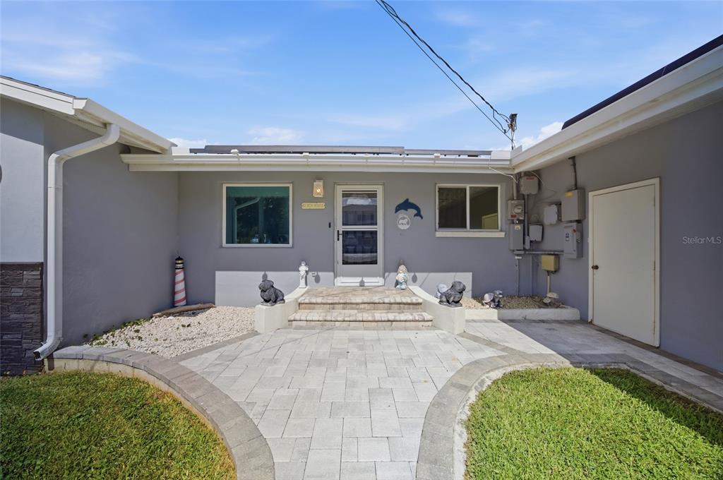 A paved walkway leads to the front entrance of a gray house with a patio — 8211 HAYWARD LANE, PORT RICHEY, FL