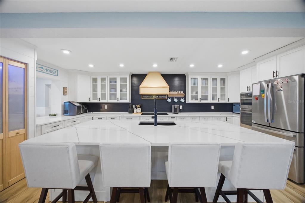 A modern kitchen features a large white quartz island, dark backsplash, and white cabinetry — 8211 HAYWARD LANE, PORT RICHEY, FL