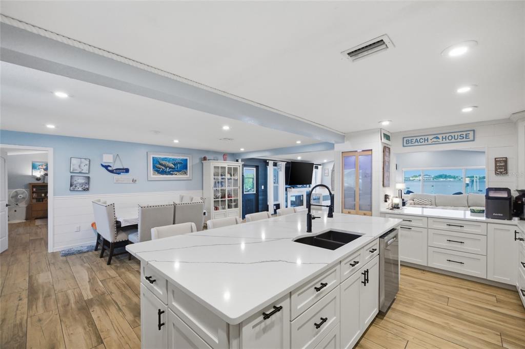 A kitchen features a large white quartz island, white cabinetry, and light wood-look flooring — 8211 HAYWARD LANE, PORT RICHEY, FL