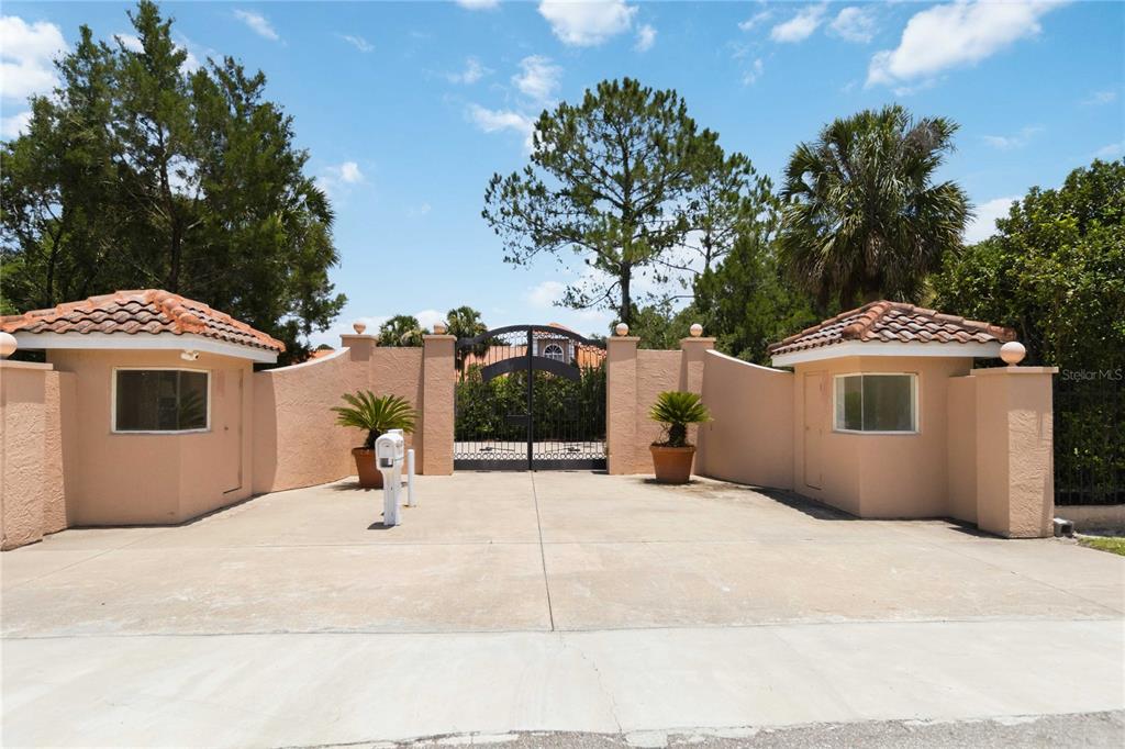A gated entrance with two guardhouses and a paved driveway under a blue sky — 593 DUNMAR CIRCLE, WINTER SPRINGS, FL
