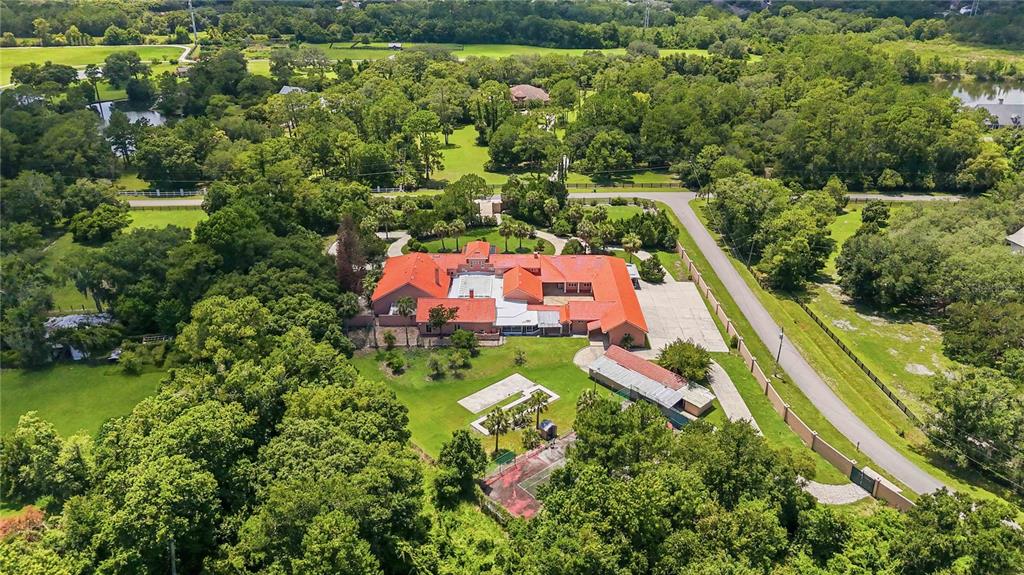 An aerial view shows a large house with a red roof, tennis court, and surrounding trees — 593 DUNMAR CIRCLE, WINTER SPRINGS, FL