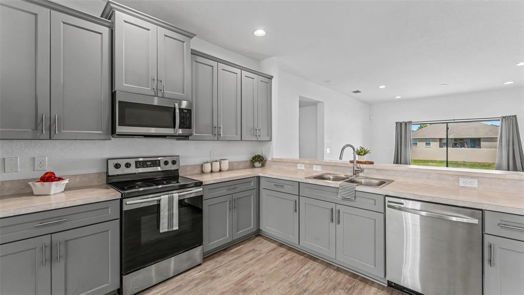 A kitchen features gray cabinets, stainless steel appliances, and a view into an adjacent room — 2728 HUDSON STREET, LAKELAND, FL