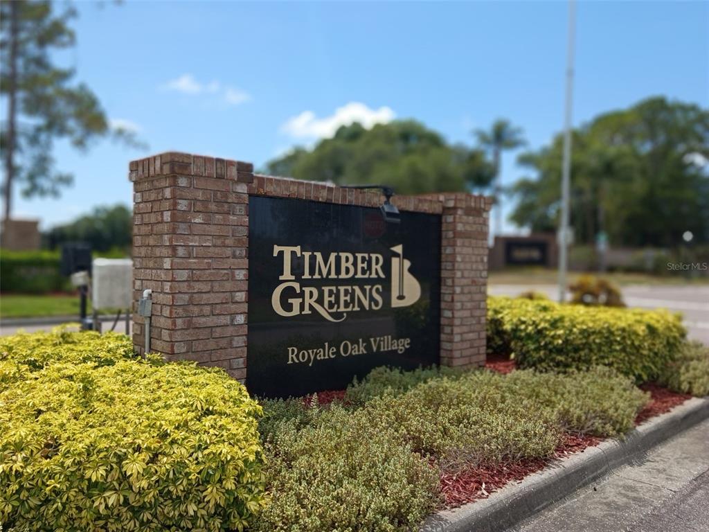 A gated community entrance features a small guardhouse, a stone waterfall, and lush trees — 10029 BROOKDALE DRIVE, NEW PORT RICHEY, FL