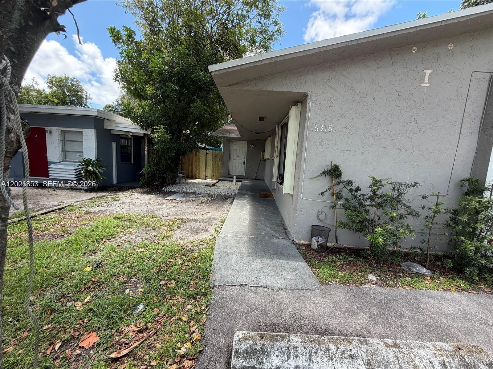A concrete walkway leads to the entrance of a gray stucco building with a flat roof — 6316 Lincoln St, Hollywood FL 33024, HOLLYWOOD, FL