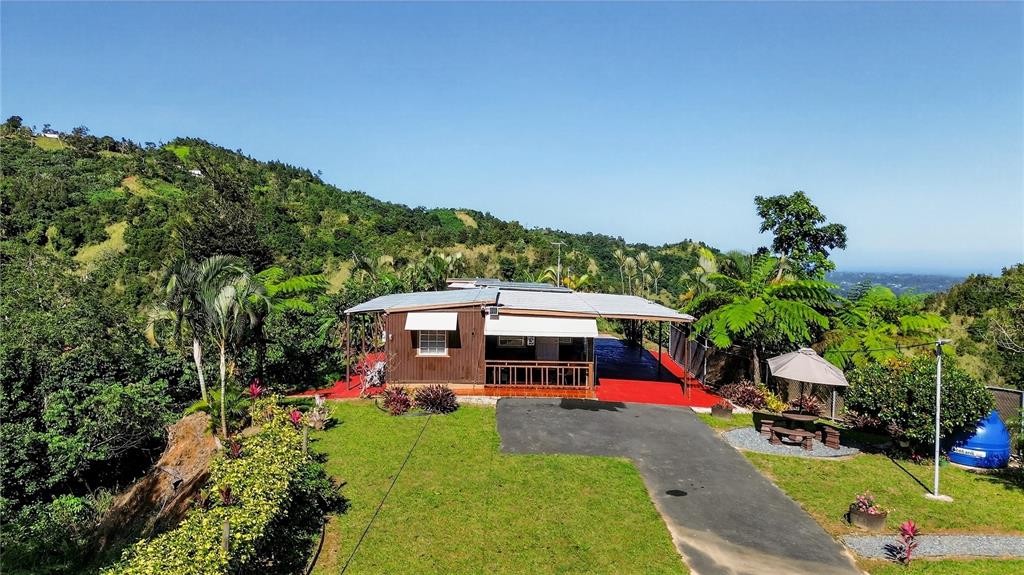 A single-story house with a red patio sits on a grassy hill overlooking mountains — ALTURITAS CACAO PARCEL B, OROCOVIS, PR