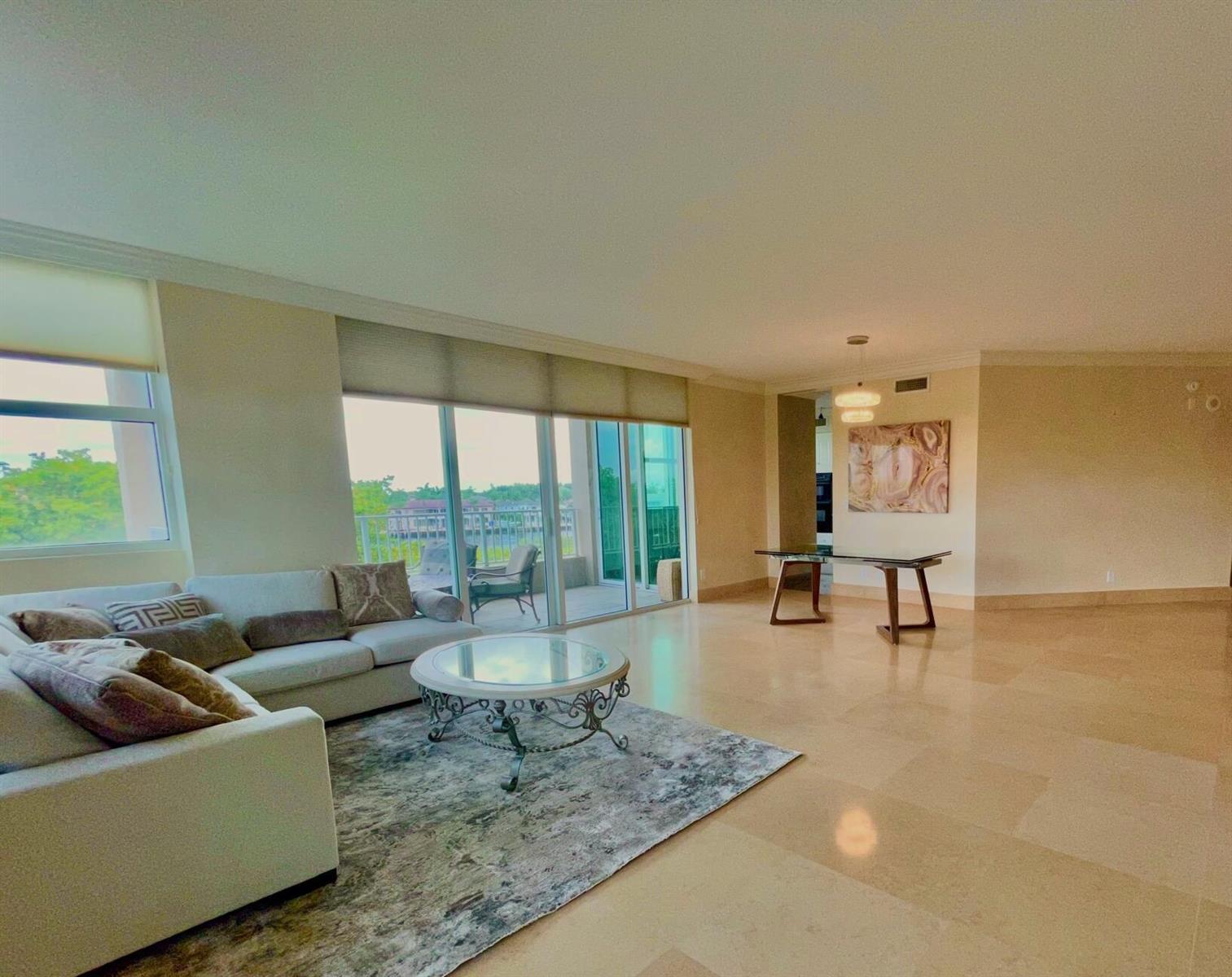 A spacious living room with tile floors, a white sofa, and glass sliding balcony doors — 3720 S Ocean Boulevard # 301b, Highland Beach FL 33487, HIGHLAND BEACH, FL