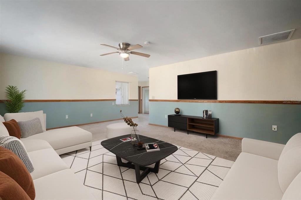 This virtually staged living room features a white sectional sofa, a black coffee table, and a television — 609 FOX HILLS DRIVE, SUN CITY CENTER, FL