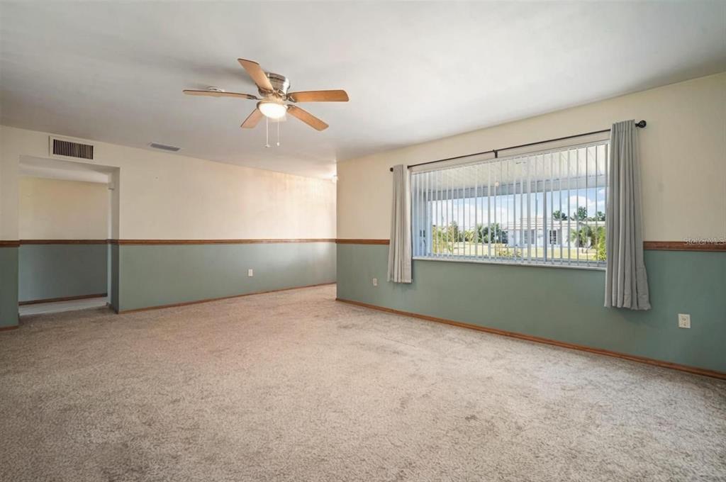 An empty living room features beige carpet, two-toned walls, a ceiling fan, and large windows — 609 FOX HILLS DRIVE, SUN CITY CENTER, FL