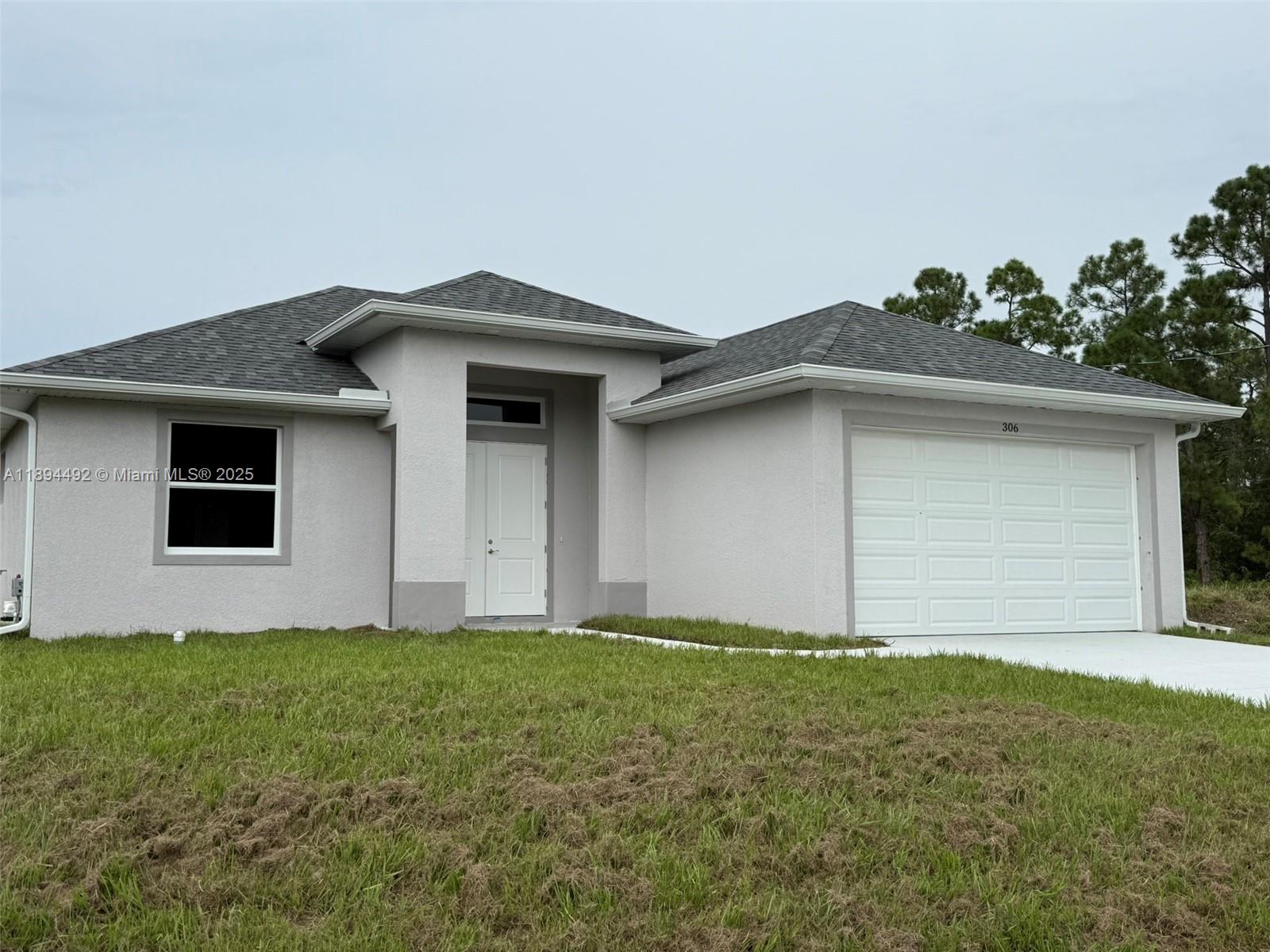 A single-story house with a gray stucco exterior, a two-car garage, and a dark roof — 306 Lenz Ave S, Lehigh Acres FL 33974, LEHIGH ACRES, FL