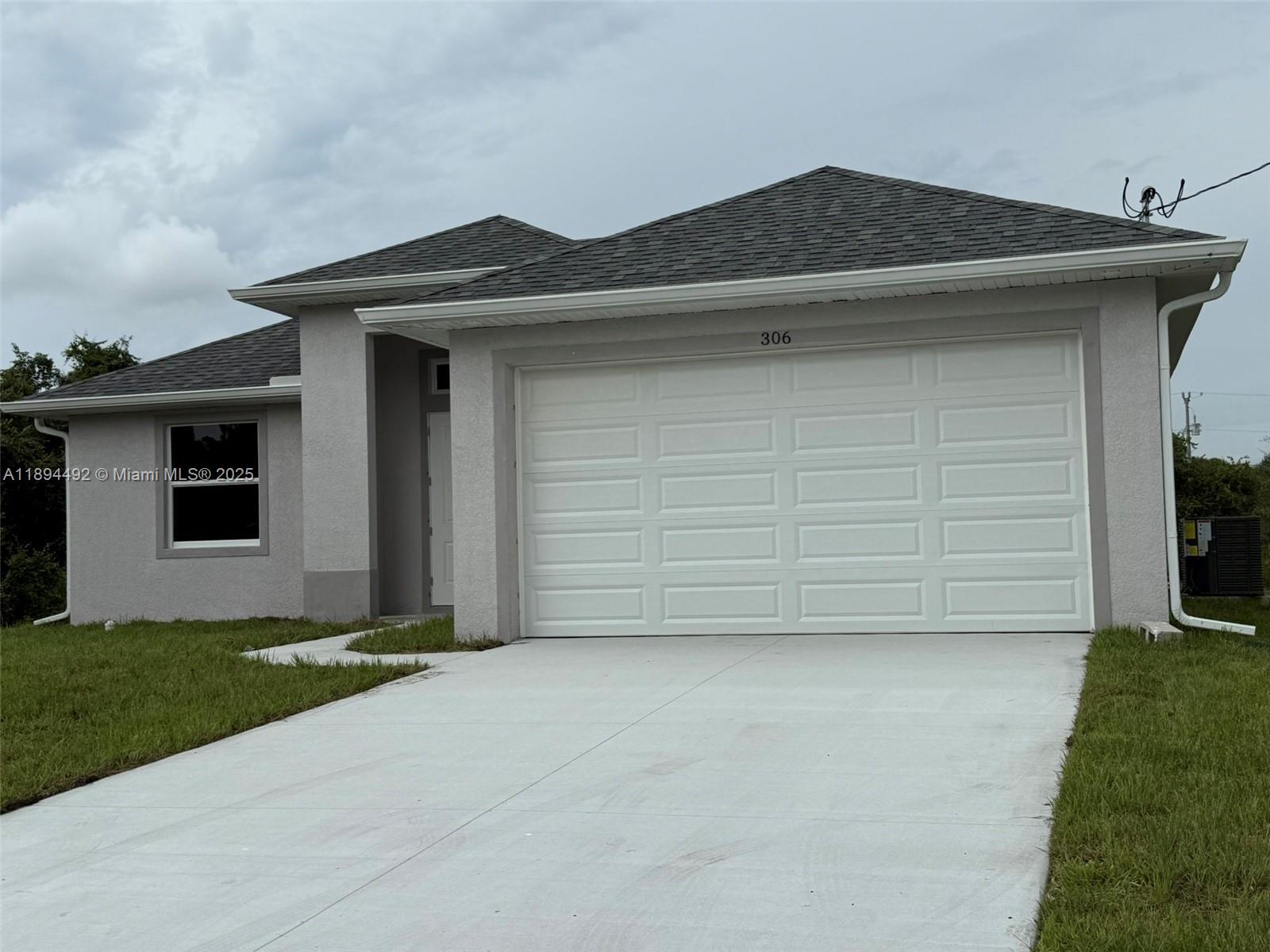 A single-story house with a gray stucco exterior, a white garage door, and a driveway — 306 Lenz Ave S, Lehigh Acres FL 33974, LEHIGH ACRES, FL