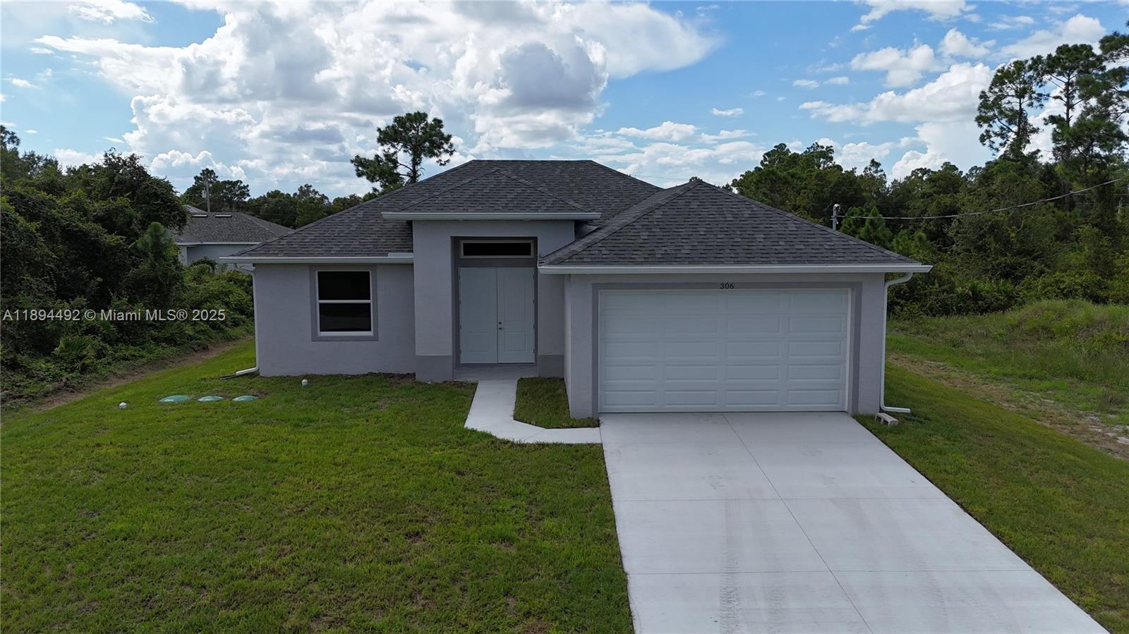 A single-story house with a gray exterior, a two-car garage, and a concrete driveway — 306 Lenz Ave S, Lehigh Acres FL 33974, LEHIGH ACRES, FL