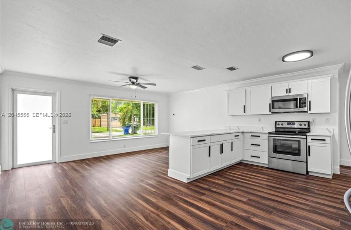 A white kitchen with stainless steel appliances opens into a living area with wood floors — 6321 Thomas St, Hollywood FL 33024, HOLLYWOOD, FL