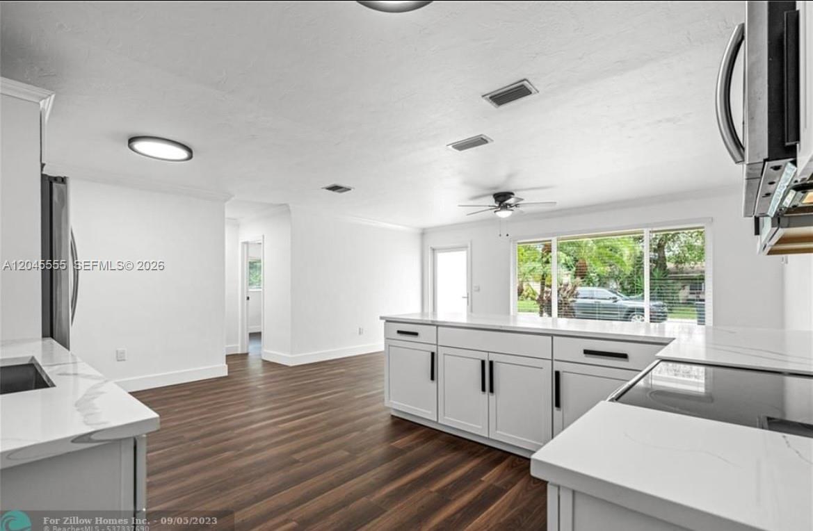 A modern kitchen features white cabinetry, marble-style countertops, and dark wood-look flooring — 6321 Thomas St, Hollywood FL 33024, HOLLYWOOD, FL