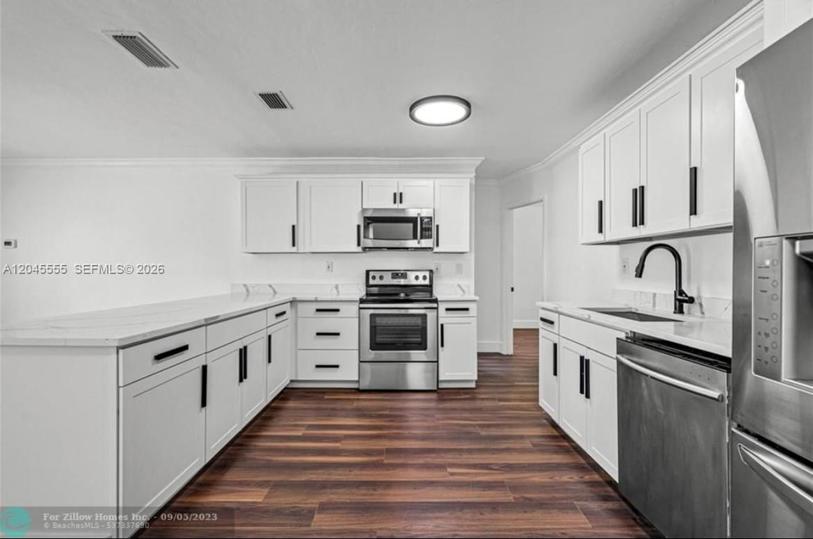 A modern kitchen features white cabinets, stainless steel appliances, and dark wood-look flooring — 6321 Thomas St, Hollywood FL 33024, HOLLYWOOD, FL