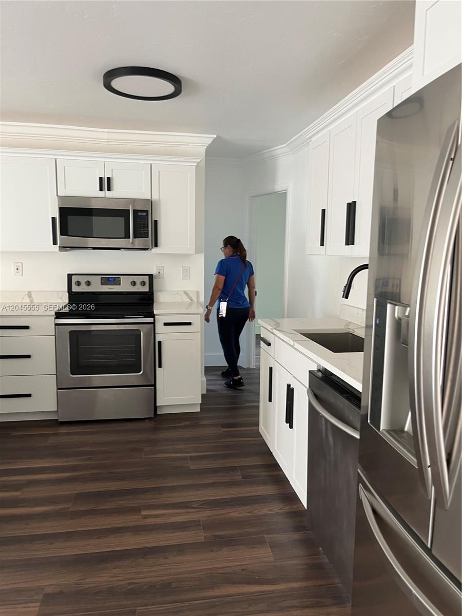 A kitchen features white cabinets, stainless steel appliances, and dark wood-look flooring — 6321 Thomas St, Hollywood FL 33024, HOLLYWOOD, FL