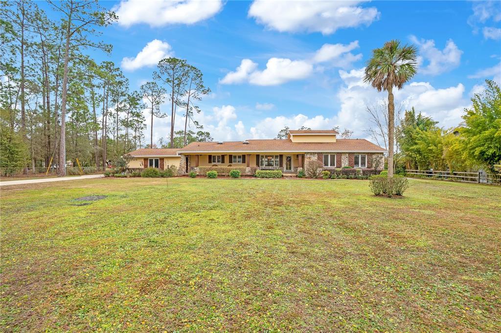 A single-story house with a stone facade and a large front lawn under a blue sky — 11450 FANGORN ROAD, ORLANDO, FL
