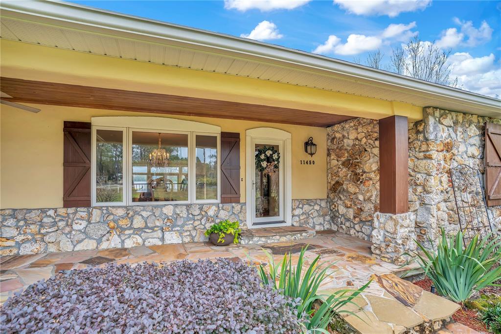 A stone-faced house exterior features a covered porch, a bay window, and a front door — 11450 FANGORN ROAD, ORLANDO, FL