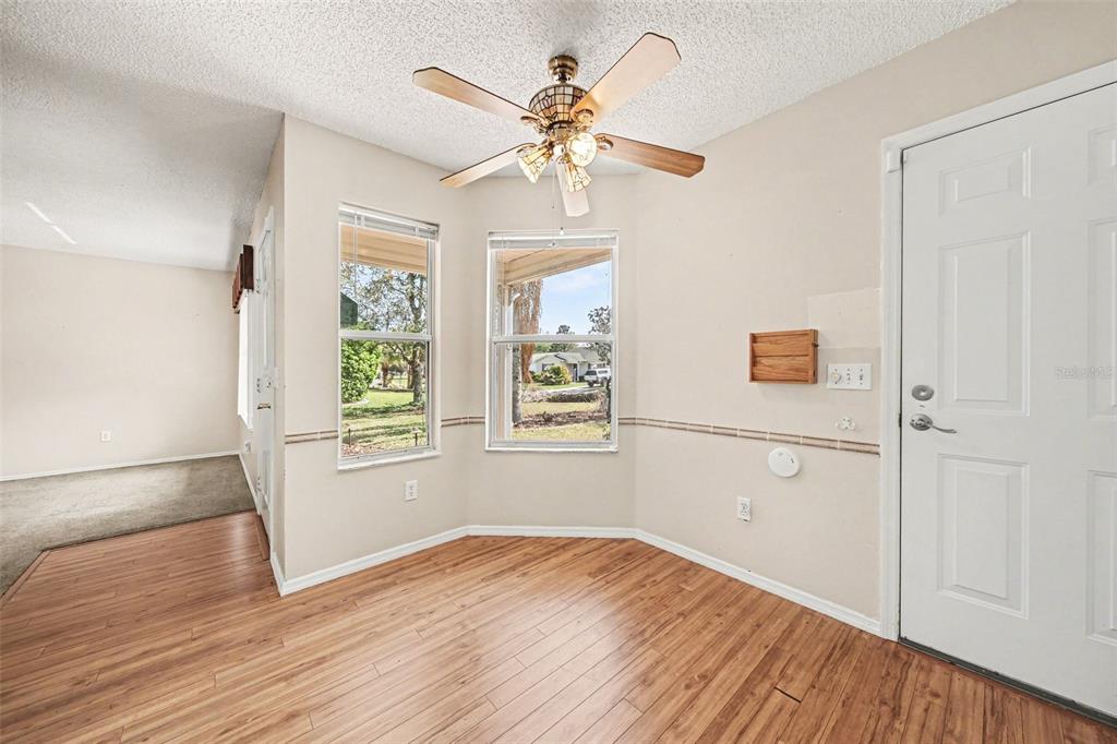 A dining area features wood-look flooring, a ceiling fan, and two windows overlooking a yard — 1239 CHAPARRAL DRIVE, THE VILLAGES, FL
