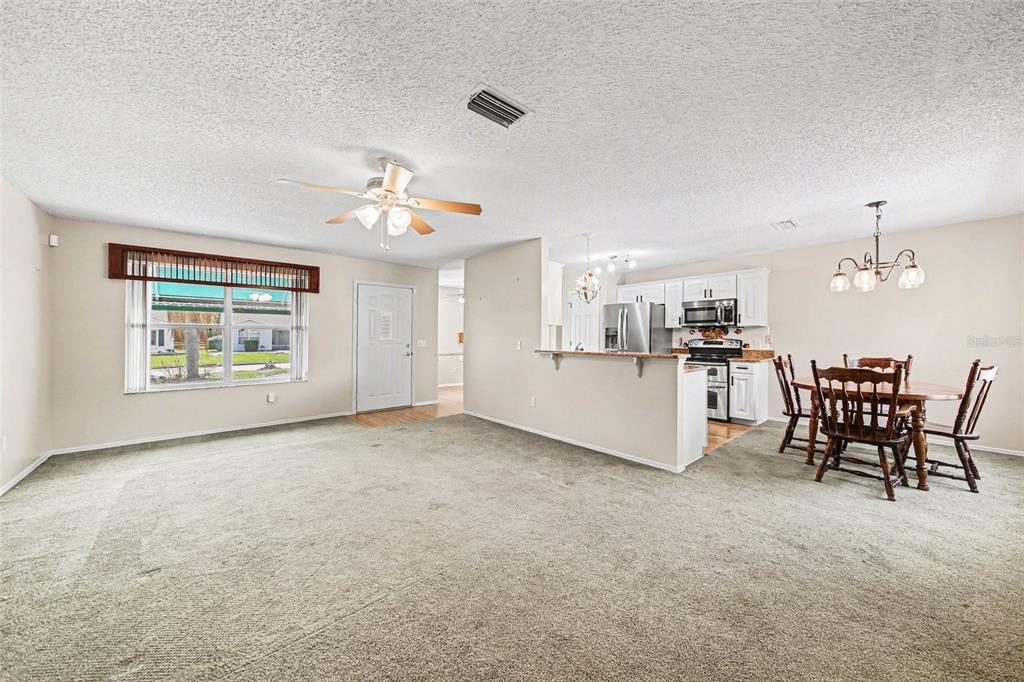 An open-concept living and dining area features wall-to-wall carpeting, a ceiling fan, and kitchen access — 1239 CHAPARRAL DRIVE, THE VILLAGES, FL