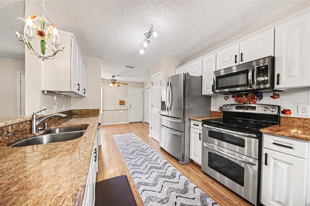 A kitchen with white cabinets, granite countertops, stainless steel appliances, and a patterned runner rug — 1239 CHAPARRAL DRIVE, THE VILLAGES, FL