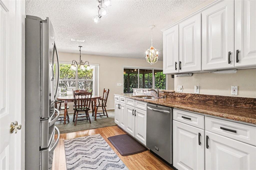 A kitchen with white cabinets, granite countertops, stainless steel appliances, and an adjacent dining area — 1239 CHAPARRAL DRIVE, THE VILLAGES, FL