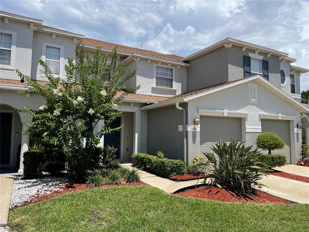 A two-story townhouse exterior features a beige facade, two garage doors, and a front garden — 2508 HASSONITE STREET, KISSIMMEE, FL