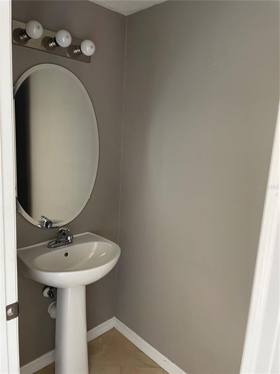 A small bathroom features a pedestal sink, an oval mirror, and a three-bulb vanity light — 2508 HASSONITE STREET, KISSIMMEE, FL