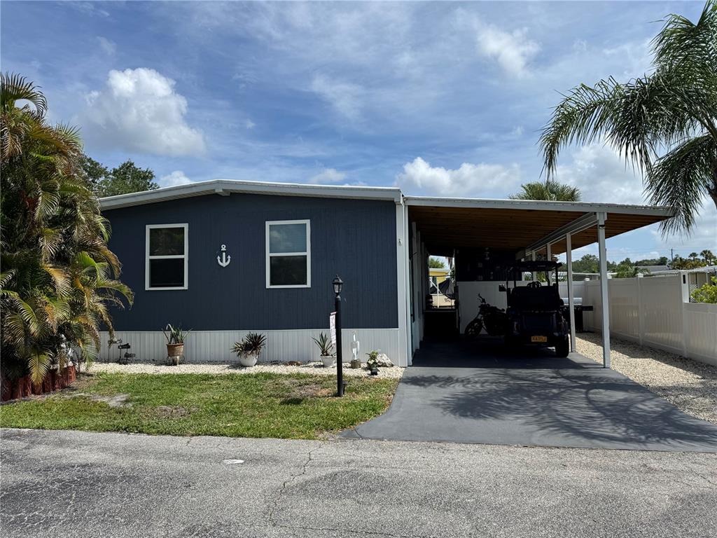 A blue manufactured home features a carport, a golf cart, and a small anchor decoration — 420 49TH STREET E UNIT 45, PALMETTO, FL