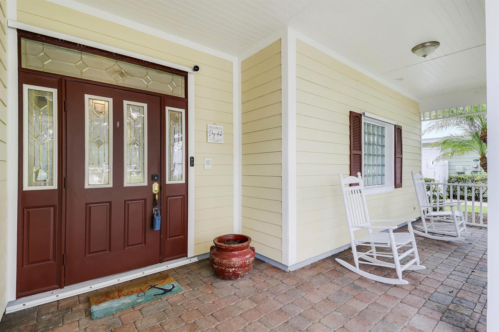 A covered front porch features a red door, two white rocking chairs, and brick flooring — 654 NE Little Kayak Point, FL 34983, FL