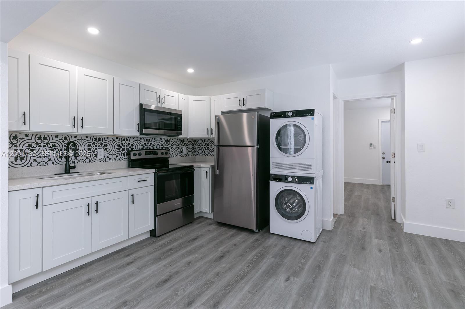A kitchen features white cabinets, stainless steel appliances, a patterned backsplash, and a stacked washer-dryer — 6125 SW 40th Ct # 4, Miramar FL 33023, MIRAMAR, FL
