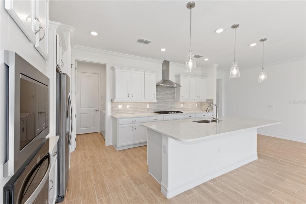 A modern white kitchen features a large island, stainless steel appliances, and light wood-look flooring — 4559 NW 53RD AVENUE ROAD, OCALA, FL
