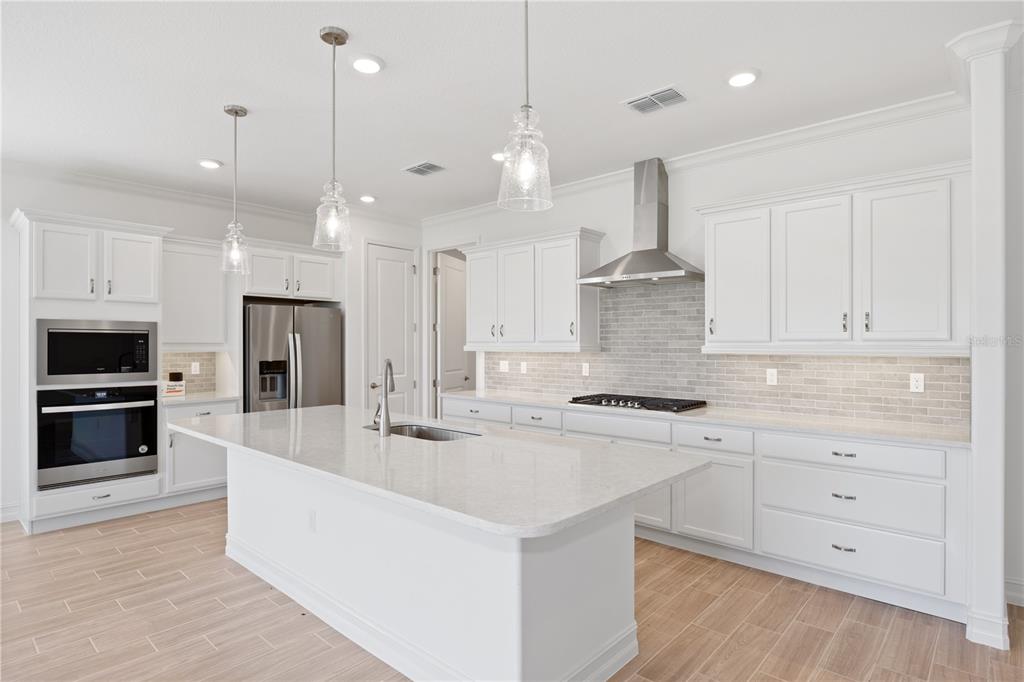 A modern kitchen features white cabinetry, a large quartz island, stainless steel appliances, and tile flooring — 4559 NW 53RD AVENUE ROAD, OCALA, FL