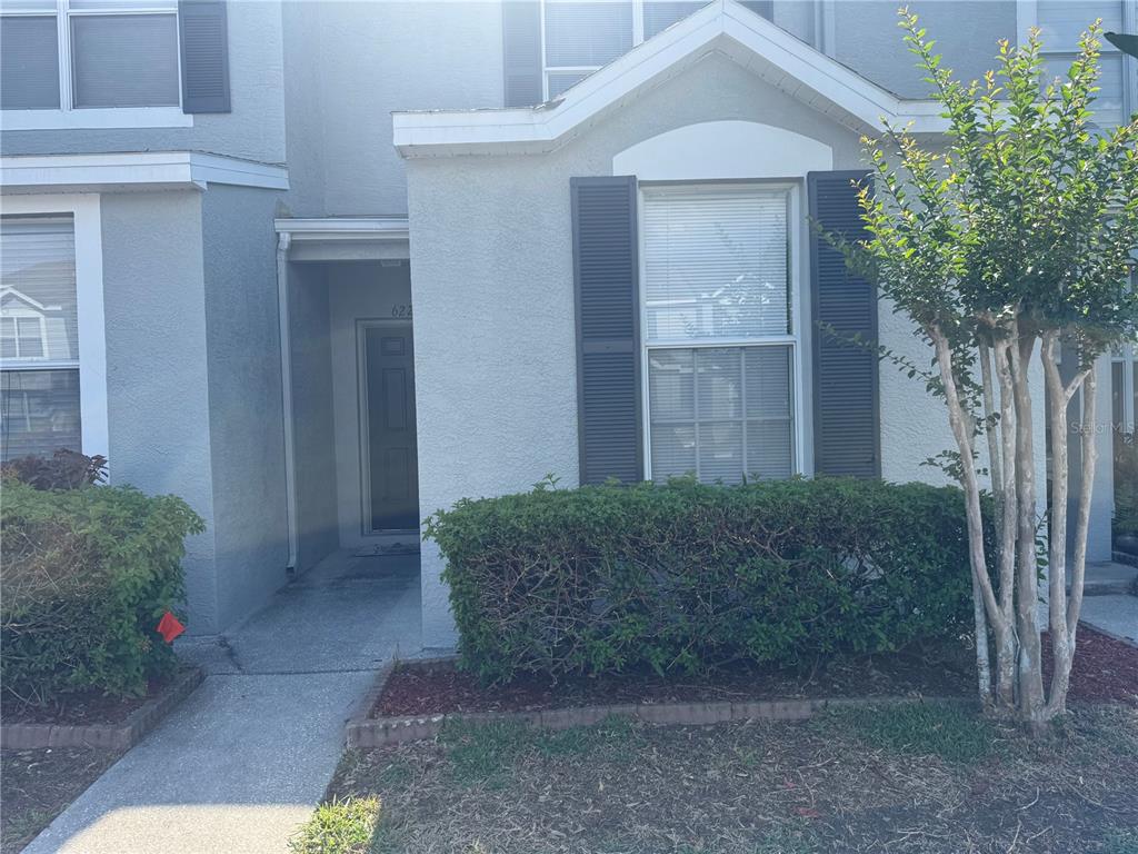 A two-story townhouse exterior features a recessed entryway, gray stucco siding, and a front hedge — 6229 OSPREY LAKE CIRCLE, RIVERVIEW, FL