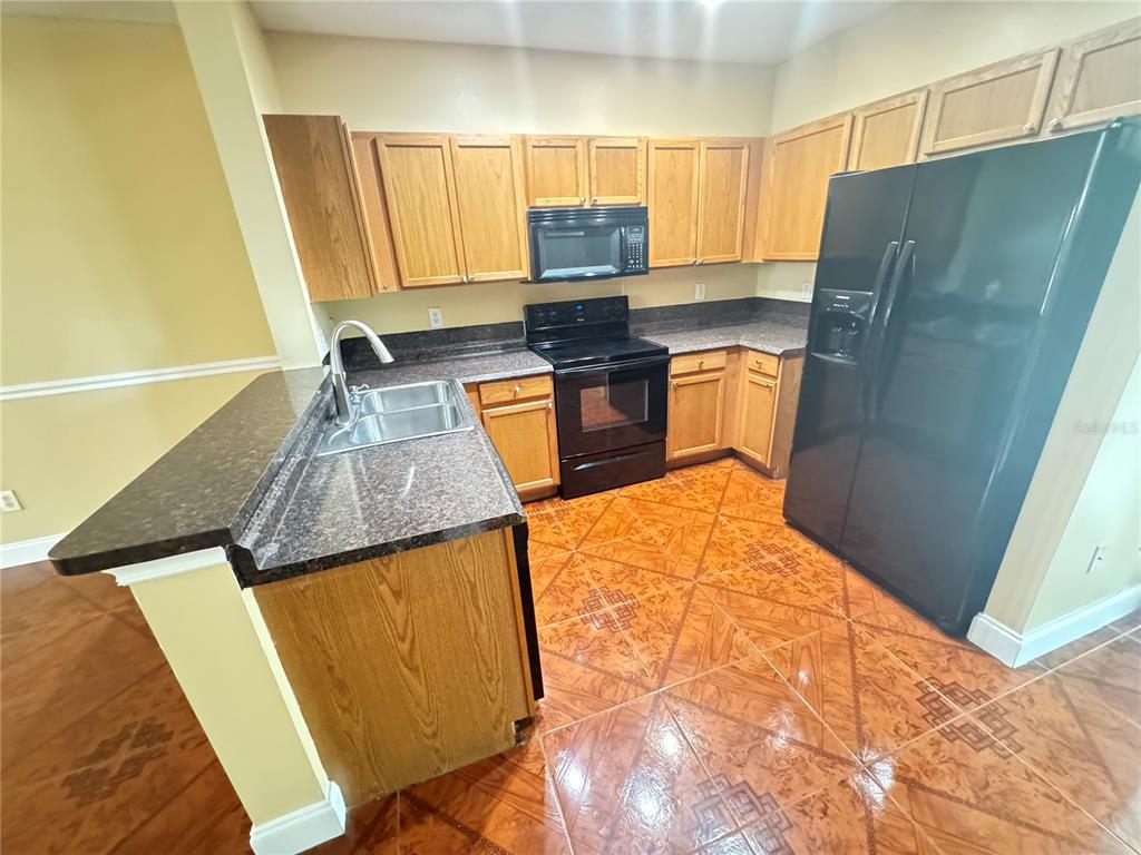 A kitchen features oak cabinets, dark countertops, black appliances, and patterned tile flooring — 6229 OSPREY LAKE CIRCLE, RIVERVIEW, FL