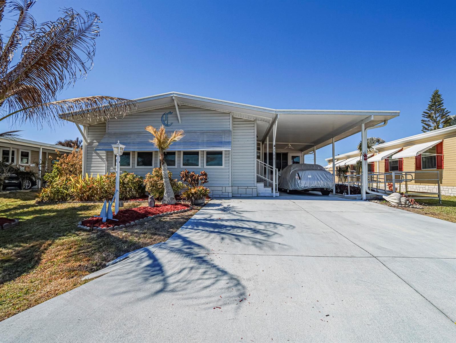A light-colored manufactured home features a concrete driveway, a carport, and a small front garden — 7566 Montauk Avenue # U19, FL 32976, FL