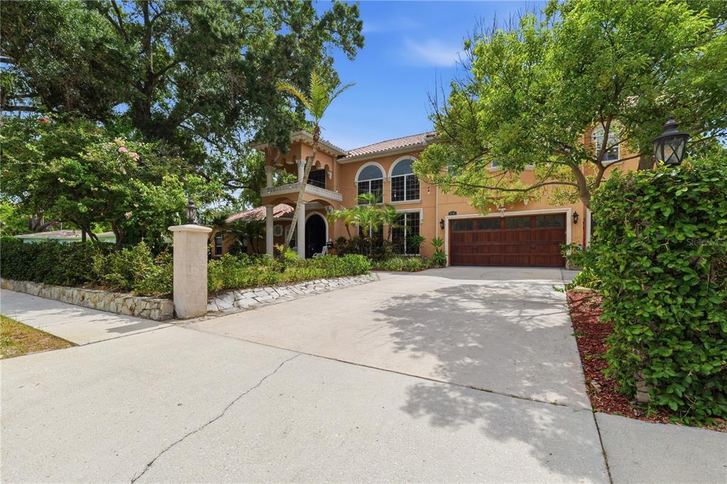 A two-story stucco house with a wooden garage door and a stone-walled front garden — 10307 RECLINATA LANE, TAMPA, FL