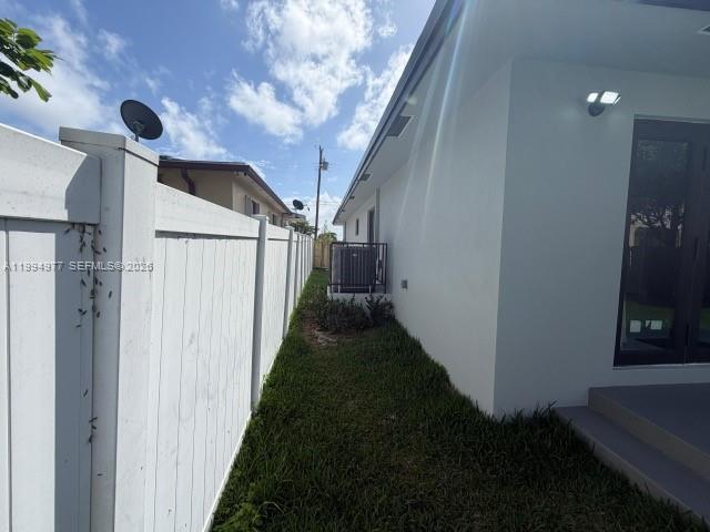 A white fence runs alongside the exterior wall of a modern house with a yard — 644 NW 6th Ct, Hallandale Beach FL 33009, HALLANDALE BEACH, FL
