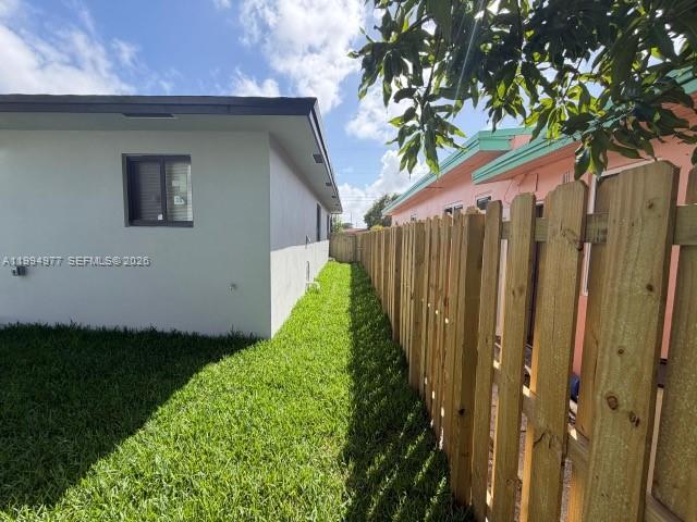 A side view of a house exterior with a wooden fence and green lawn — 644 NW 6th Ct, Hallandale Beach FL 33009, HALLANDALE BEACH, FL