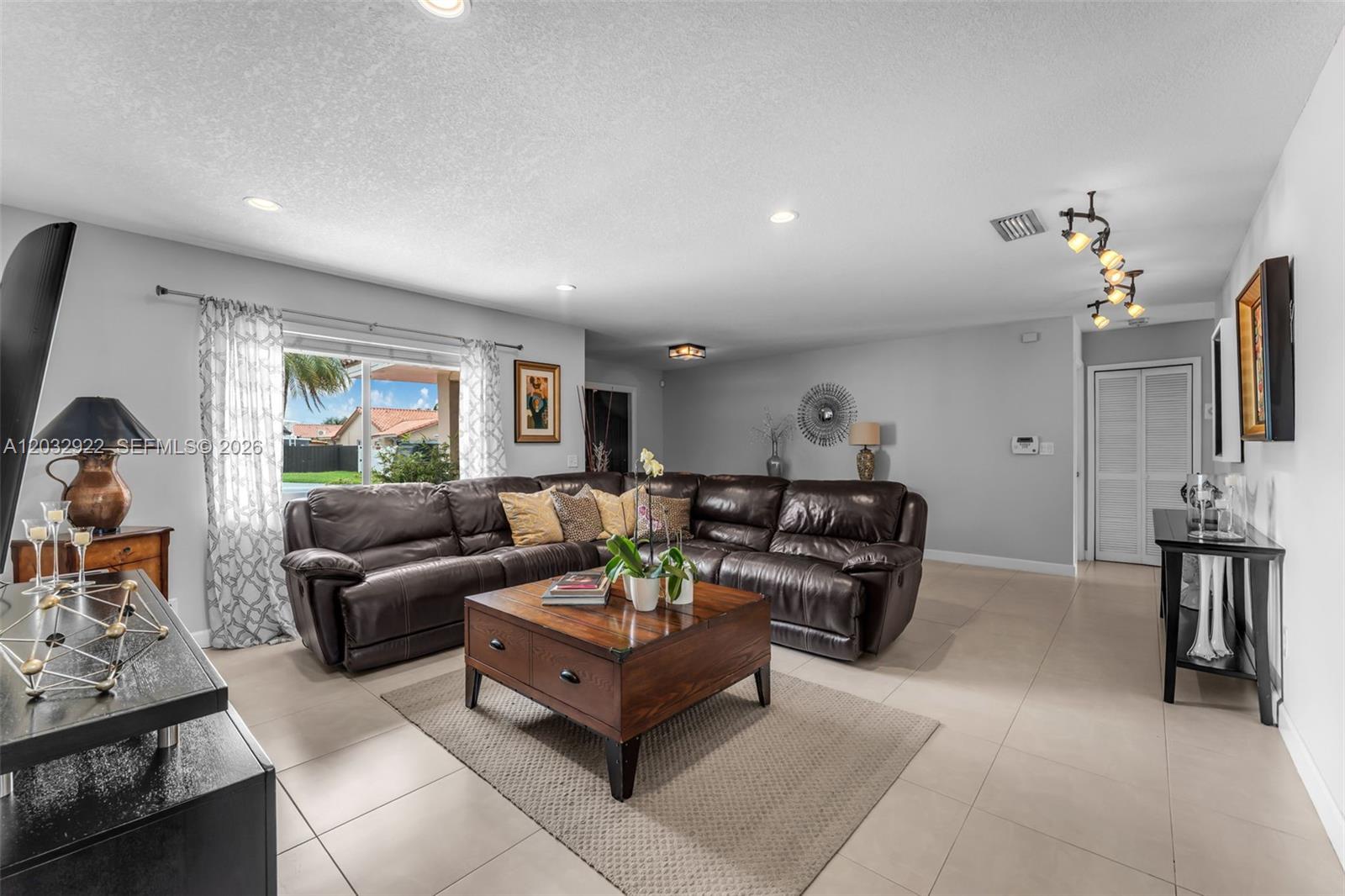 A living room features a large brown leather sectional, a wooden coffee table, and tile flooring — 14061 SW 39th St, Miami FL 33175, MIAMI, FL