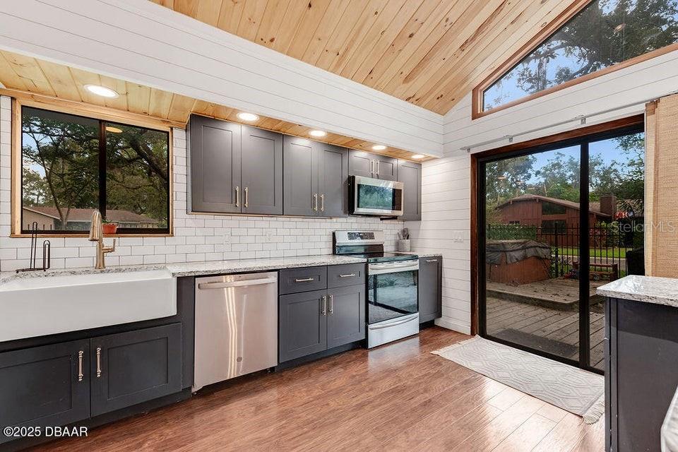 A modern kitchen features dark gray cabinets, white subway tile, and a wood-paneled vaulted ceiling — 28 BAYMEADOW COURT, ORMOND BEACH, FL