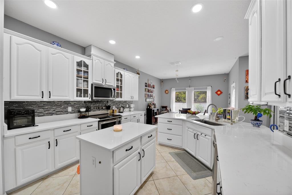 A kitchen features white cabinets, a central island, quartz countertops, and light tile flooring — 3651 DAYDREAM PLACE, ST CLOUD, FL