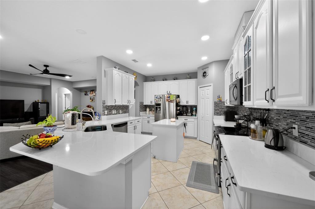 A bright kitchen features white cabinets, quartz countertops, a center island, and tile flooring — 3651 DAYDREAM PLACE, ST CLOUD, FL