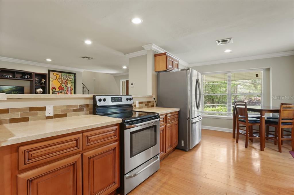 A kitchen features wood cabinets, stainless steel appliances, a tile backsplash, and light-colored countertops — 200 CROOKED OAK COURT, LONGWOOD, FL