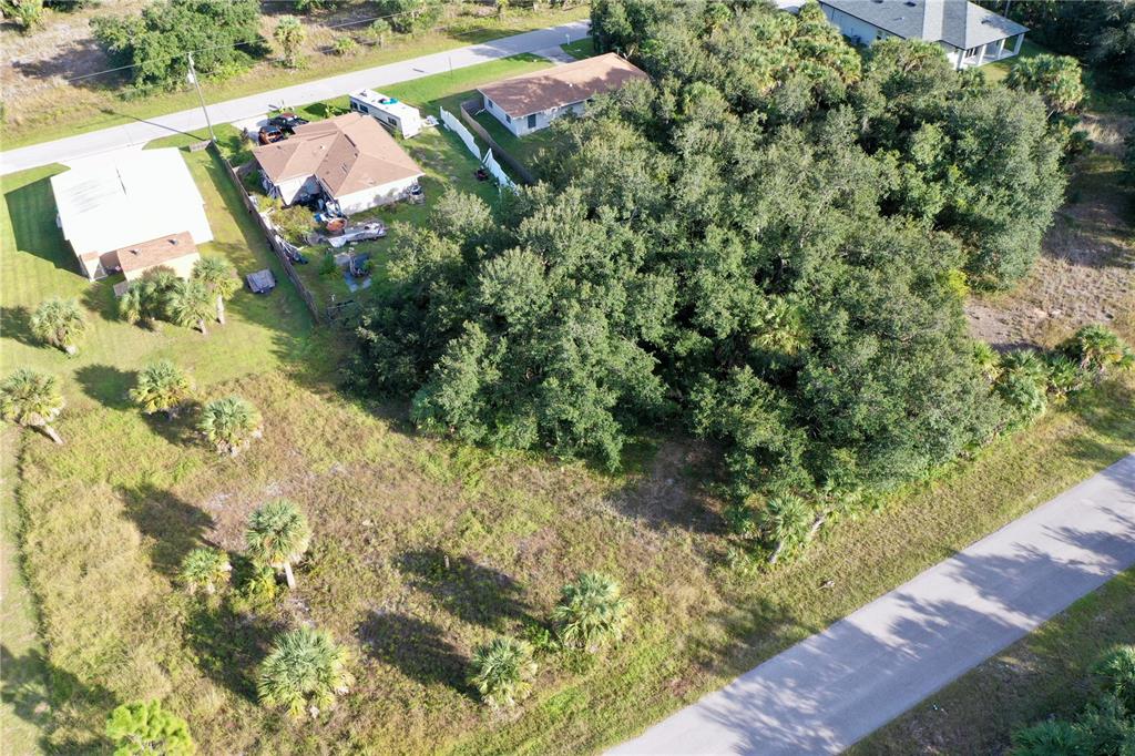 An aerial view shows a vacant grassy lot adjacent to a wooded area and houses — 454 LEONA STREET, PORT CHARLOTTE, FL