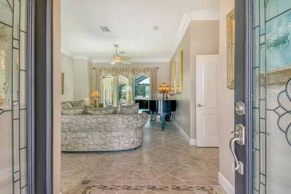 A view through a decorative glass front door into a living room with a grand piano — 9477 CEDAR RIDGE LANE, SARASOTA, FL