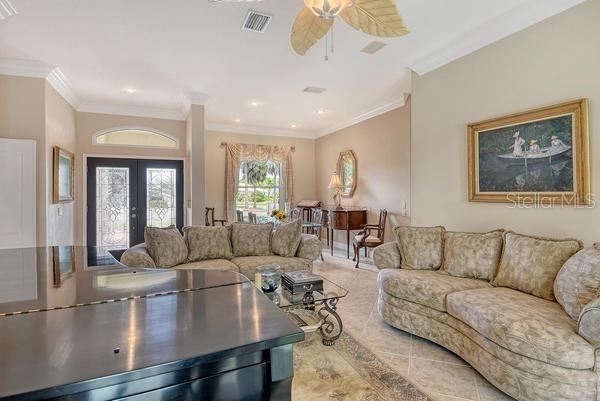 A living room features a grand piano, patterned sofas, and a dining area in the background — 9477 CEDAR RIDGE LANE, SARASOTA, FL